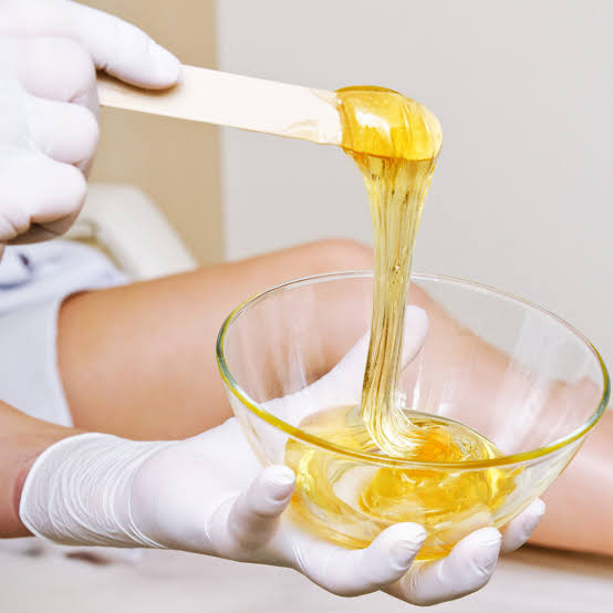 Mãos com luvas preparando cera depilatória em uma tigela
